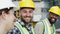 Three frontline workers wearing hard hats and high-visibility vests chatting at work, with an audio waveform representing frontline employee communication.